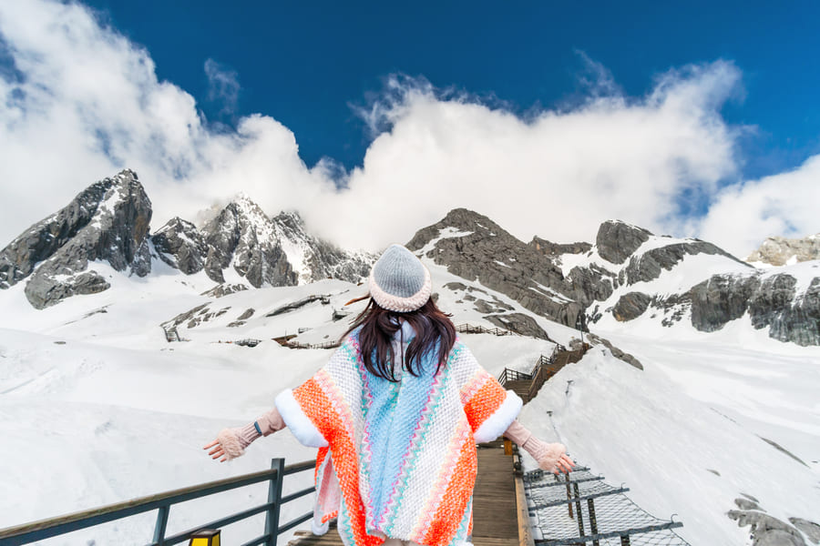 Fondo de montanas cubiertas de nieve y una mujer de espaldas en el medio usando un sombrero y